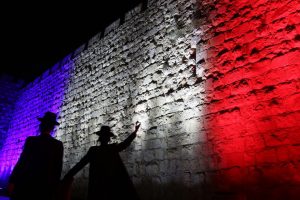 Israeli Ultra Orthodox Jewish men walk past Jerusalem's Old City Ottoman Walls illuminated in red, white and blue, the colors of the French flag, in Jerusalem on November 15, 2015 in solidarity with France and the attacks in Paris. Islamic State jihadists claimed a series of coordinated attacks by gunmen and suicide bombers in Paris that killed at least 129 people in scenes of carnage at a concert hall, restaurants and the national stadium Paris. 
