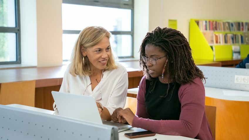 young ethnic female student doing assignment with tutor in university